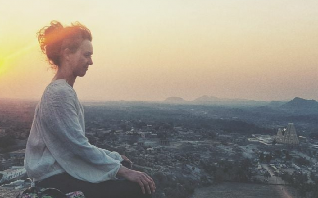 Anika sitzt vor einem Sonnenuntergang in Meditation